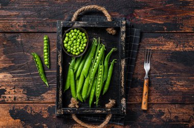 Tahta tepside çiğ bezelye kabukları. Koyu ahşap arka plan. Üst görünüm