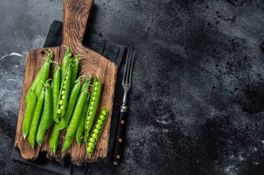Taze bezelyeler ve yeşil bezelye kabukları ahşap bir kesme tahtasında. Siyah arka plan. Üst Manzara. Boşluğu kopyala