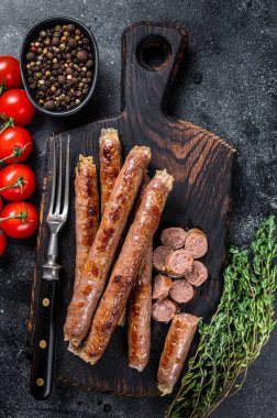 Ahşap bir tahtanın üzerinde kızarmış et sosisi, otlar ve domatesle. Siyah arka plan. Üst görünüm