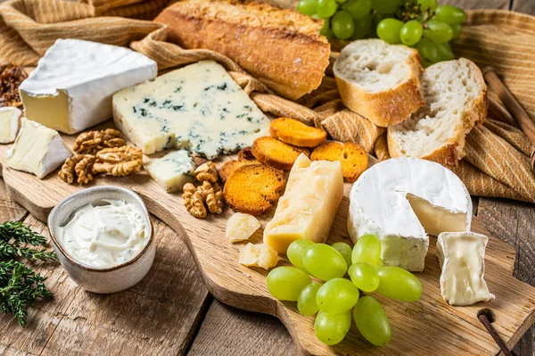 Tábua de queijo. Brie, Camembert, Roquefort, parmesão e creme de queijo azul com uva, figo, pão e nozes em tábua de madeira. fundo de madeira. Vista superior — Fotografia de Stock