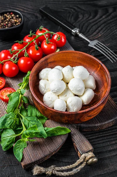 İtalyan küçük Mozzarella peynir topları, fesleğen ve domates kirazı Caprese salatası pişirmeye hazır. Siyah ahşap arka plan. Üst görünüm