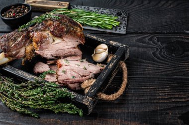 Ahşap bir tepside et satırıyla dilimlenmiş kızarmış koyun eti bacağı. Siyah ahşap arka plan. Üst Manzara. Boşluğu kopyala