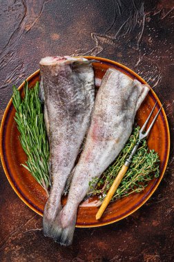 Pişmemiş çiğ morina ya da kırsal tabakta otlu ve çatallı morina balığı. Karanlık arka plan. Üst görünüm