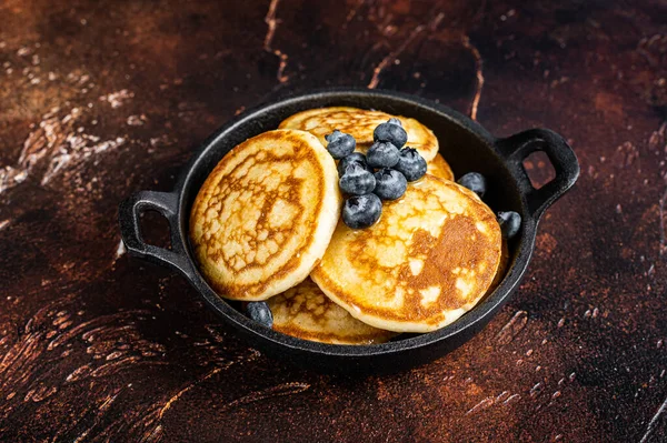 Gebratene Pfannkuchen mit frischen Blaubeeren und Ahornsirup in einer Pfanne. Dunkler Hintergrund. Ansicht von oben — Stockfoto