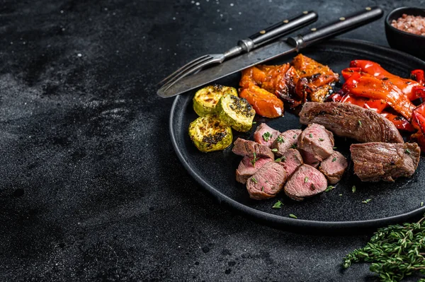 Filet d'agneau ou de chèvre rôti Steak de viande dans une assiette avec légumes grillés. Fond en bois noir. Vue de dessus. Espace de copie — Photo