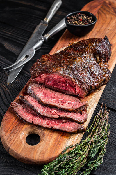 Grilled Butchers choice steak Onglet Hanging Tender beef meat on a cutting board. Black wooden background. Top View.