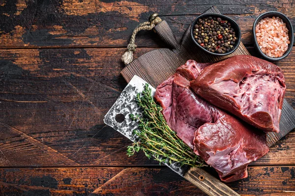 Raw sliced Beef or veal heart on a cutting board with meat cleaver. Dark wooden background. Top View. Copy space — Stock Photo, Image