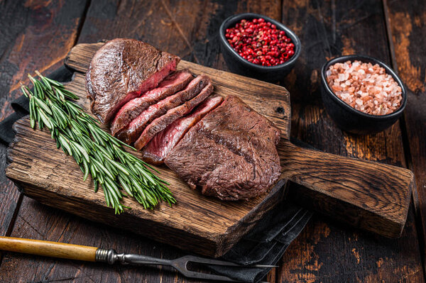 Fried Top Blade or flat iron roast beef meat steaks on wooden board with rosemary. Dark wooden background. Top View
