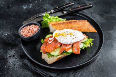 Benedict yumurtalı sandviç tostu, füme somon ve ekmekle avokado. Siyah arka plan. Üst görünüm