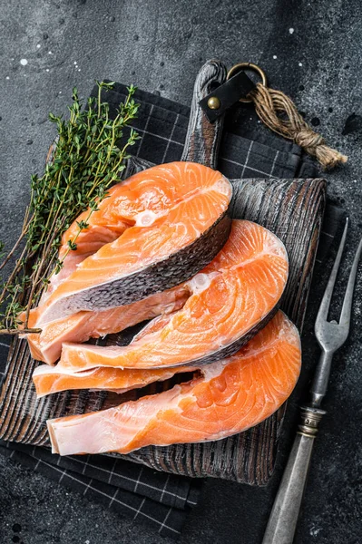 Syrové lososy nebo pstruhy, ryby připravené k vaření na dřevěné desce. Černé pozadí. Horní pohled — Stock fotografie
