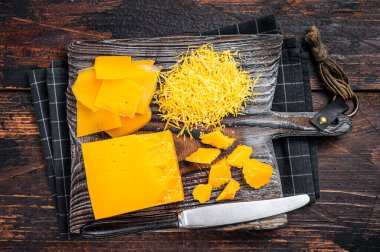 Tahta bir tahtanın üzerinde rendelenmiş ve oyulmuş Cheddar Cheese. Koyu ahşap arka plan. Üst görünüm