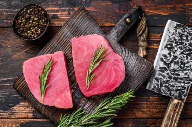 Tahta kesme tahtasında satırla çiğ ton balığı bifteği. Koyu ahşap arka plan. Üst görünüm