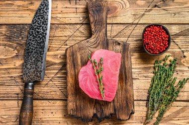 Tahta kesme tahtasında bıçakla taze çiğ ton balığı bifteği. Ahşap arka plan. Üst görünüm