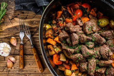 Biftek eti ve sebze yahnisi siyah fırın kabında. Ahşap arka plan. Üst görünüm