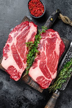 Çiğ Chuck göz devirme bifteği kesme tahtasının üzerinde birinci sınıf et. Siyah arka plan. Üst görünüm