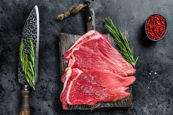 Raw fresh beef meat round steak with herbs and spices. Black background. Top view