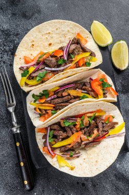 Biftek, soğan, domates ve tatlı biberli Meksika taco kabuğu. Siyah arka plan. Üst görünüm