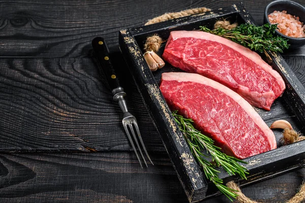 Bistecca di picanha brasiliana cruda o bistecca di carne di manzo con filetto in un vassoio di legno. Fondo in legno nero. Vista dall'alto. Copia spazio — Foto Stock