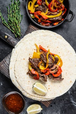 Meksika Fajitası, renkli biber ve soğanlı, tortilla ve salsa ile servis ediliyor. Siyah arka plan. Üst görünüm