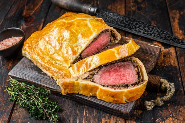 Homemade Beef Wellington puff pie with tenderloin meat on a cutting board. Dark wooden background. Top view