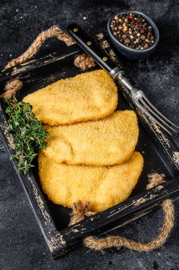 Tahta tepside otlarla birlikte çiğ tavuk cordon bleu et pirzolası. Siyah arka plan. Üst görünüm