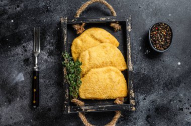 Tahta tepside otlarla birlikte çiğ tavuk cordon bleu et pirzolası. Siyah arka plan. Üst görünüm