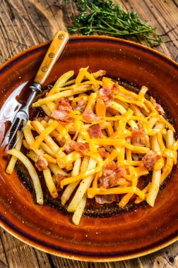 Kızarmış patates kızartması, erimiş çedar peyniri ve domuz pastırması, köy tabağında servis ediliyor. Ahşap arka plan. Üst görünüm