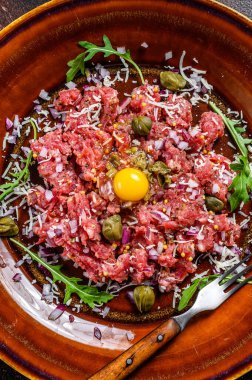 Çiğ yumurta sarısı, turşu ve parmesan peynirli biftek tartar. Karanlık arka plan. Üst görünüm