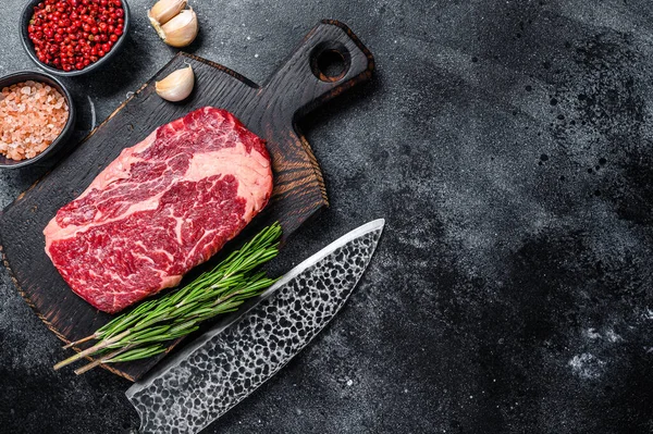 Černý angus ribeye, syrový steak z hovězího žebra na dřevěné desce s nožem. Černé pozadí. Horní pohled. Kopírovat prostor — Stock fotografie