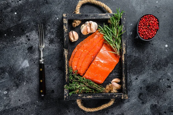 Gerookte gesneden zalmfilet in een houten dienblad met kruiden. Zwarte achtergrond. Bovenaanzicht — Stockfoto