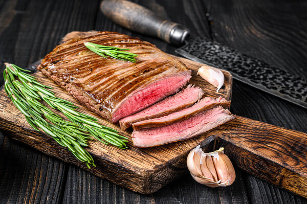 BBQ Grilled flank or flap beef meat steak on a wooden cutting board. Black wooden background. Top view.