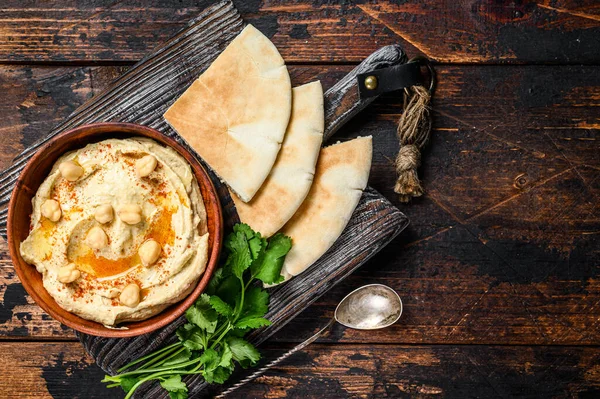 Hummus paste with pita bread, chickpea and parsley in a wooden bowl. Dark wooden background. Top view. Copy space — Stock Photo, Image