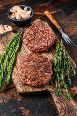 Tahta bir kesme tahtasının üzerinde kıyma etinden hamburger için ızgara biftek köftesi. Koyu ahşap arka plan. Üst görünüm