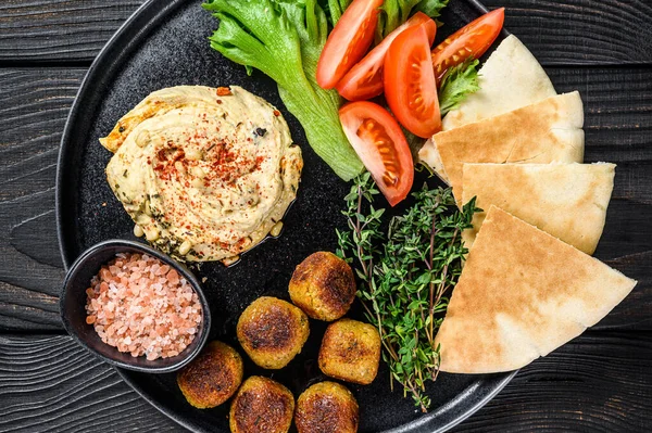 Арабська кухня Hummus chickpea, falafel, pita хліб і свіжі овочі. Чорний дерев'яний фон. Краєвид — стокове фото