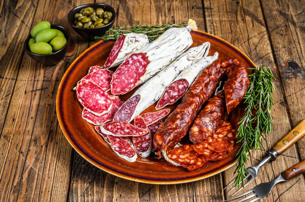 Spanish charcuterie with sliced sausages salami, fuet and chorizo on a rustic plate. wooden background. Top view