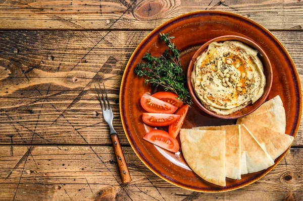 Świeży Hummus z chlebem pita, pomidorem i pietruszką na rustykalnym talerzu. drewniane tło. Widok góry. Przestrzeń kopiowania — Zdjęcie stockowe
