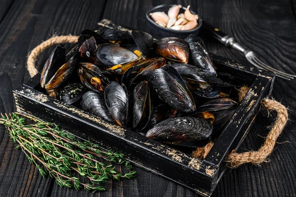 Cozze al vapore in gusci in un vassoio di legno con erbe. Fondo in legno nero. Vista dall'alto — Foto Stock