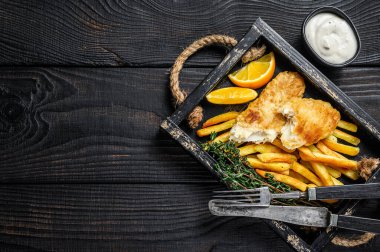 Patates kızartması ve ahşap tepside tartar soslu haşlanmış balık ve patates kızartması. Siyah ahşap arka plan. Üst Manzara. Boşluğu kopyala