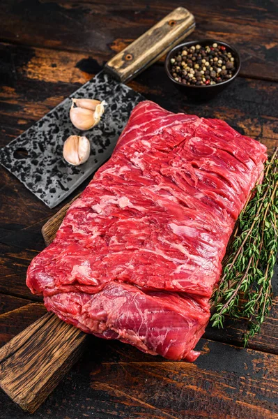 生の牛肉のブリスケットの大きな作品は、ハーブや肉屋のクリーバーと肉をカット。暗い木製の背景。トップ表示 — ストック写真