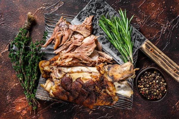 Roasted and cut German pork knuckle eisbein meat on a wooden board with meat cleaver. Dark background. Top view — Stock Photo, Image