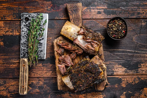 BBQ short chuck beef ribs with herbs and meat cleaver. Dark wooden background. Top view