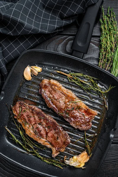 Biftecks de boeuf Angus noir Premier grillé Striploin ou New York dans une poêle à griller. Fond en bois foncé. Vue du dessus — Photo