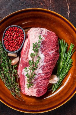 Çiğ, yuvarlak, etli et, rustik bir tabakta, otlu rosto için kesilmiş. Karanlık arka plan. Üst görünüm