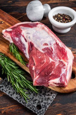 Tahta bir kasapta çiğ kuzu eti ya da keçi omuzu eti, satırla tahtayı keser. Koyu ahşap arka plan. Üst görünüm