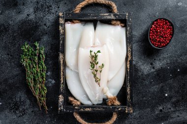 Ahşap tepside otlu çiğ beyaz mürekkep balığı ya da kalamar. Siyah arka plan. Üst görünüm