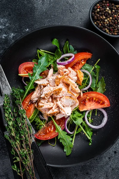 Saláta sült lazac filé steak, friss saláta arugula és paradicsom egy tányéron. Fekete háttér. Felülnézet — Stock Fotó