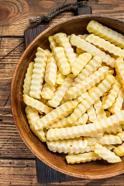 Froid Frozen Crinkle four frites pommes de terre bâtonnets dans une assiette en bois. Fond en bois. Vue du dessus — Photo