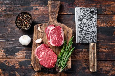 Taze çiğ fileto Mignon fileto biftekleri kasapta et satırıyla tahtayı kesiyor. Koyu ahşap arka plan. Üst görünüm