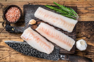 Tahta tahtada kasap bıçağıyla taze çiğ morina filetosu bifteği. Ahşap arka plan. Üst görünüm