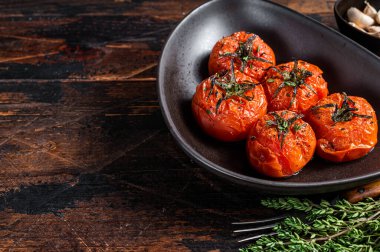 Fırında kavrulmuş kiraz domatesli kekik ve sarımsaklı bir tabak. Koyu ahşap arka plan. Üst Manzara. Boşluğu kopyala